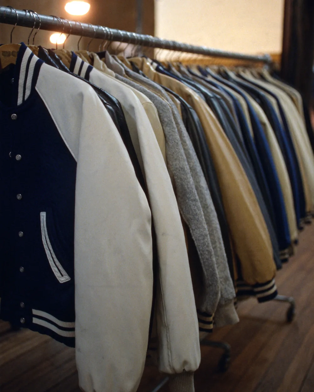 A rail of wool varsity jackets in navy and cream with white leather sleeves, hung shoulder to shoulder in a shop.